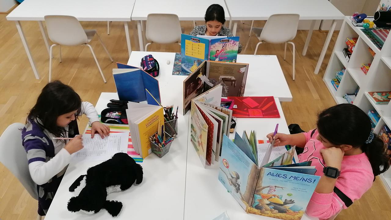 Drei Kinder sitzen am Schreibtisch und machen Schulaufgaben. Am Tisch sind viele Bücher aufgestellt.