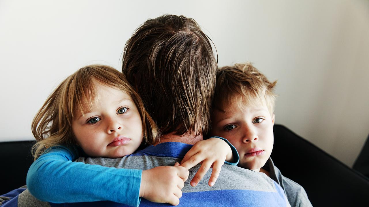 Zwei Kinder umarmen ein Elternteil und sehen traurig in die Kamera.