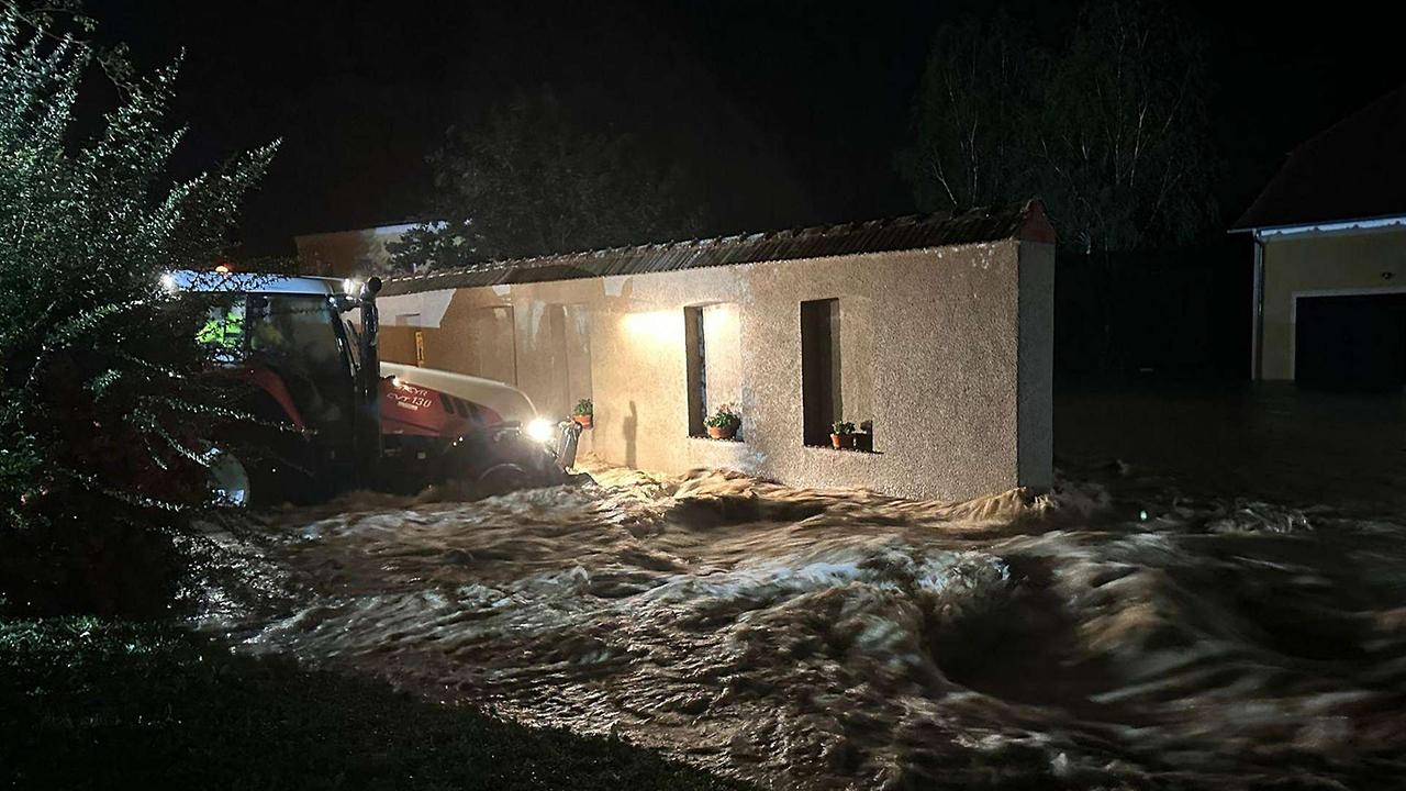 Es ist Nacht: Ein Traktor nähert sich durch die Fluten einem Haus.